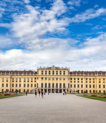 A wide-angle shot of schönbrunn palace in vienna, austria with a cloudy blue sky in the background